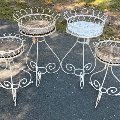 Set of four vintage white wrought iron plant stands with looped rims, scrollwork tripod bases, and round wooden insert tops, displaying...