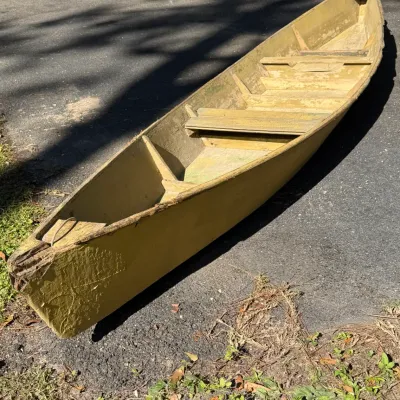 Vintage yellow painted wooden flat-bottom skiff boat featuring bench seating and weathered, distressed finish throughout.