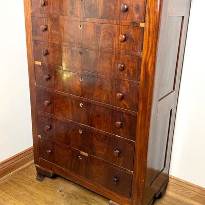 19th-century mahogany tall chest of drawers featuring flame mahogany veneer, wood knobs, and keyhole accents on ogual bracket feet.