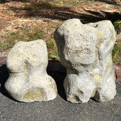 Pair of abstract concrete torso garden sculptures with weathered stone-like surfaces.