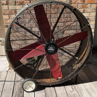 Large industrial Heat Buster barrel fan with red blades and rolling wheels, showing age-appropriate wear and surface rust.