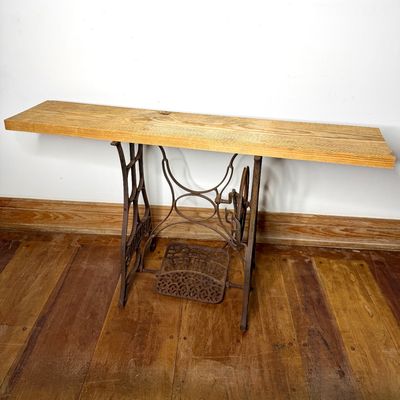 Repurposed console table crafted from an antique cast-iron treadle sewing machine base topped with a long, light oak wooden board.