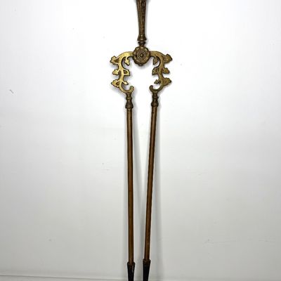 Vintage ornate brass fireplace tongs featuring decorative scrollwork and a ring top handle.