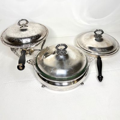 Set of vintage silver-plated chafing dishes and covered serving pans, featuring black wooden handles and ornate etched and raised details.