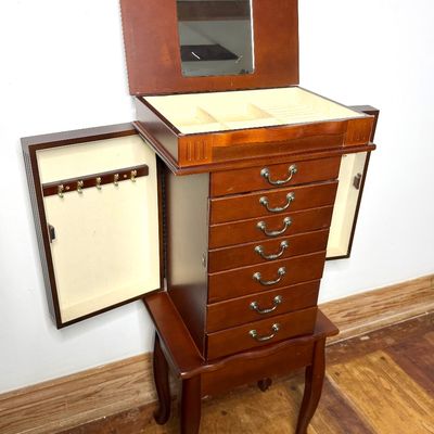 Standing wooden jewelry armoire featuring a flip-top vanity mirror, multi-tier drawers, side necklace compartments, and cabriole legs.