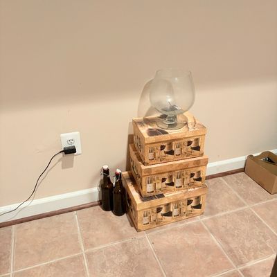 Sale Photo Thumbnail #249: Set of three wine-themed decorative storage boxes stacked on a tile floor, topped with an oversized glass snifter. Two amber swing-top glass bottles stand beside the stack.