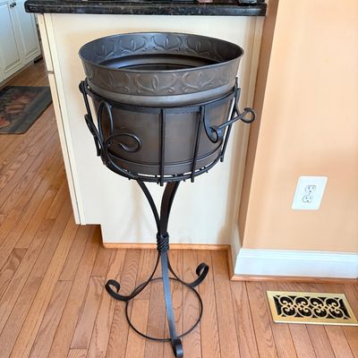 Sale Photo Thumbnail #88: Large metallic planter basin set on a black wrought-iron pedestal stand with scrolled accents.