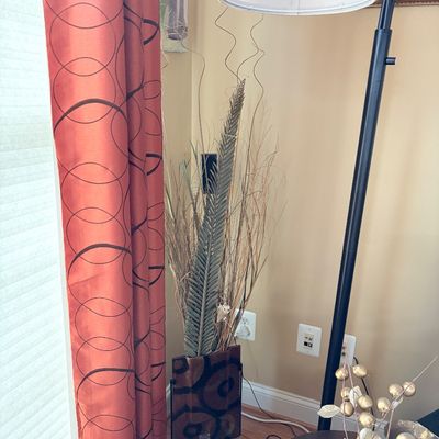 Sale Photo Thumbnail #211: A decorative floor arrangement featuring dried grasses, reeds, and a palm frond in a patterned glass vase, positioned beside burnt orange curtains and a black arc floor lamp.