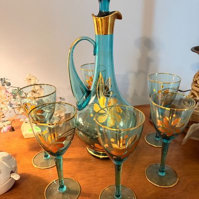 Sale Photo Thumbnail #264: Vintage teal blue glass decanter set with stopper and matching stemmed wine glasses, featuring hand-painted gold floral scrollwork accents and gilt trim.