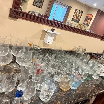 Sale Photo Thumbnail #197: Large assortment of glassware arranged on a granite countertop, including wine glasses, beer steins, rocks glasses, and branded barware.