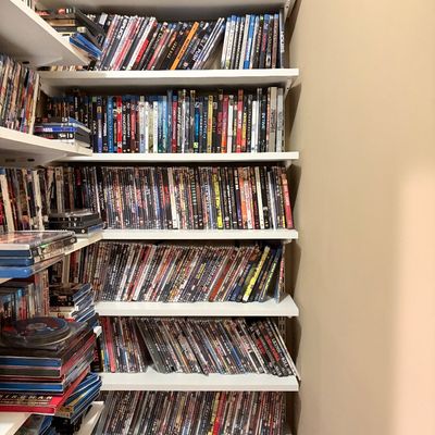Sale Photo Thumbnail #172: Large media collection featuring hundreds of DVDs and Blu-ray movies organized on white wall-mounted shelving units.