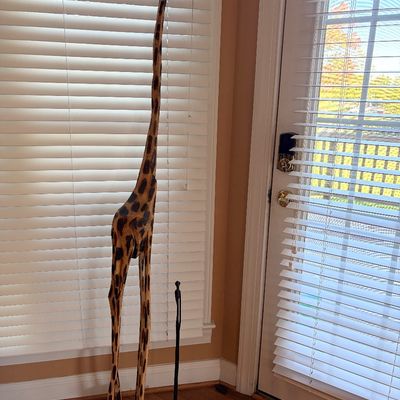 Sale Photo Thumbnail #151: Tall hand-carved wooden giraffe sculpture with painted spot details, standing alongside a smaller slender metal figurine.
