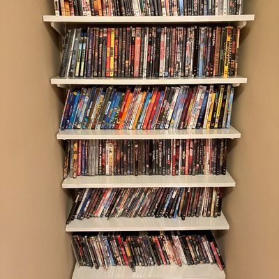 Sale Photo Thumbnail #169: Seven white wall-mounted shelves filled with a large collection of DVDs and Blu-ray movies.
