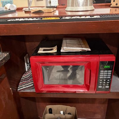 Sale Photo Thumbnail #196: Compact red microwave oven with digital display tucked under a wooden counter shelf.