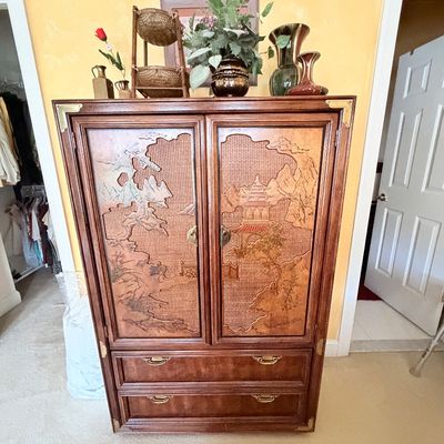 Sale Photo Thumbnail #284: Asian-inspired wooden armoire featuring carved landscape door panels, woven textured backgrounds, brass corner brackets, and two bottom drawers.
