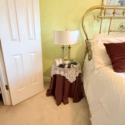 Sale Photo Thumbnail #288: A brushed metal table lamp sitting on a draped round nightstand next to a traditional brass headboard bed.