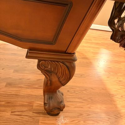 Sale Photo Thumbnail #241: Detail view of a wooden pool table featuring a carved ball-and-claw leg and leather drop pocket with fringe.