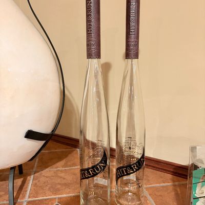 Sale Photo Thumbnail #193: Pair of empty Hit & Run baseball bat-shaped Dominican rum glass bottles featuring faux-leather wrapped necks and wooden knob stoppers.