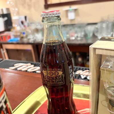 Sale Photo Thumbnail #164: Commemorative 1996 Coca-Cola glass bottle celebrating 100 years of Olympic tradition, unopened with original liquid and cap.
