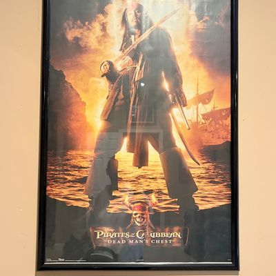 Sale Photo Thumbnail #221: Framed movie poster for Pirates of the Caribbean: Dead Man's Chest featuring Captain Jack Sparrow, encased in a slim black frame.