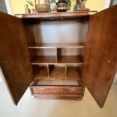Sale Photo Thumbnail #283: Traditional wooden armoire with open double doors, internal shelving compartments, a bottom drawer, and brass campaign-style corner hardware.