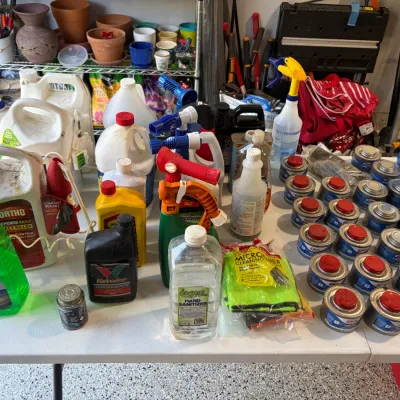 Sale Photo Thumbnail #85: Large assortment of household cleaning supplies, automotive fluids, garden chemicals, and Sterno canned heat cans arranged on a folding table.