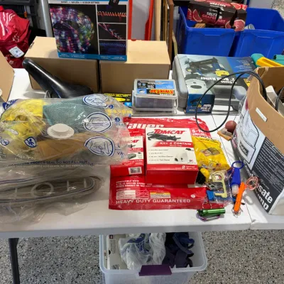 Sale Photo Thumbnail #83: Assorted household and workshop items arranged on a folding table, including LED strip lights, a brad nailer in its case, Tomcat pest control traps, and a condensate removal pump.
