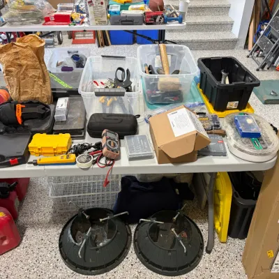 Sale Photo Thumbnail #81: A table arranged with various hand tools, power tools, plastic storage bins, gas cans, and a boxed projector screen.