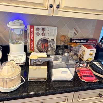 Sale Photo Thumbnail #91: Collection of kitchen appliances and accessories including a KitchenAid blender, citrus juicer, electric can opener, knife block set, and various cookware items arranged on a granite countertop.