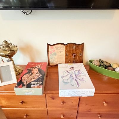 Sale Photo Thumbnail #294: Wooden dresser top featuring vintage boxed Barbie dolls including Shopping Chic Barbie and Classique Starlight Dance Barbie, a brass lamp, framed clock, picture frame, and decorative bowl.
