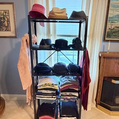 Sale Photo Thumbnail #271: Black metal rolling storage rack organized with various men's and women's hats, folded clothing, and hanging garments.