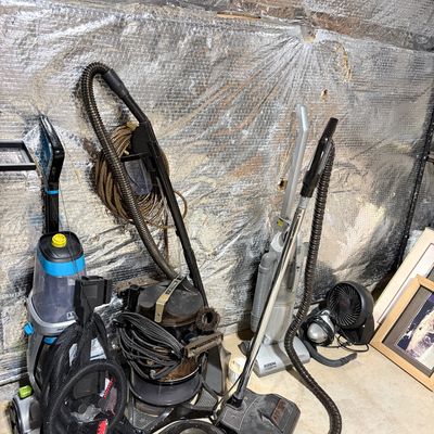 Sale Photo Thumbnail #203: Assortment of floor cleaning appliances, including a modern Bissell ProHeat carpet cleaner alongside vintage canister vacuum cleaners, hoses, and attachments.