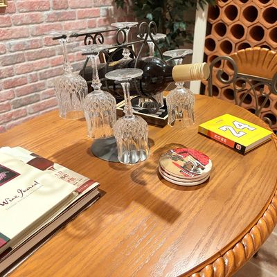 Sale Photo Thumbnail #247: Round wooden table featuring a wrought iron wine bottle and glass caddy, cut crystal stemware, coasters, and coffee table books.