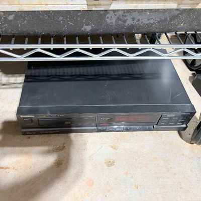 Sale Photo Thumbnail #204: Vintage Technics SL-P101 compact disc player in black casing, stored under a wire shelf.