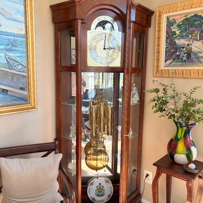Sale Photo Thumbnail #129: Traditional wooden grandfather clock featuring a swan-neck pediment, brass face with moon phase dial, and glass display side panels.