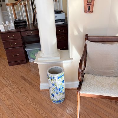 Sale Photo Thumbnail #131: Cylindrical ceramic umbrella stand with a blue floral motif, set alongside an upholstered wooden armchair and a dark wood executive desk.