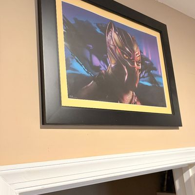 Sale Photo Thumbnail #218: Framed Marvel Black Panther wall art print, featuring Killmonger's Golden Jaguar suit, matted in yellow and set in a thick black wood frame.