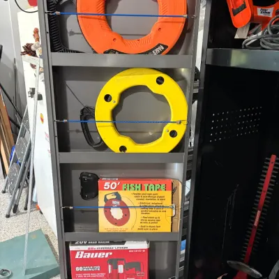 Sale Photo Thumbnail #55: Metal shelving unit containing fish tapes, including Klein Tools and GB Electrical brands, alongside a boxed Bauer 20V cordless brad nailer.