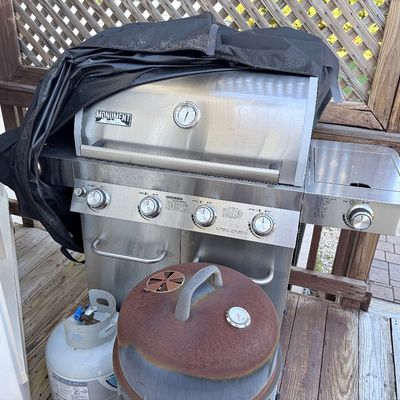 Sale Photo Thumbnail #93: Monument Grills stainless steel four-burner propane gas grill with a side burner and protective cover, accompanied by a propane tank and a rusted kettle grill lid.