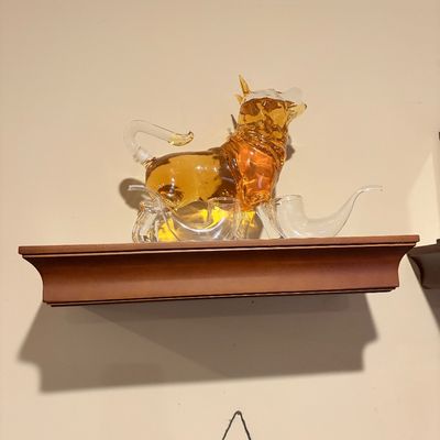 Sale Photo Thumbnail #191: Novelty glass bull decanter set filled with amber liquid, displayed on a wooden wall shelf.