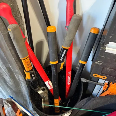 Sale Photo Thumbnail #26: Collection of modern long-handled gardening loppers and pruning tools, including Fiskars and Corona brands, stored in a black bucket.