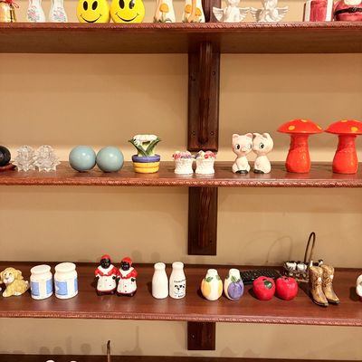 Sale Photo Thumbnail #181: Collection of novelty ceramic salt and pepper shakers displayed on wooden wall shelves, featuring various mid-century, holiday, animal, and fruit designs.