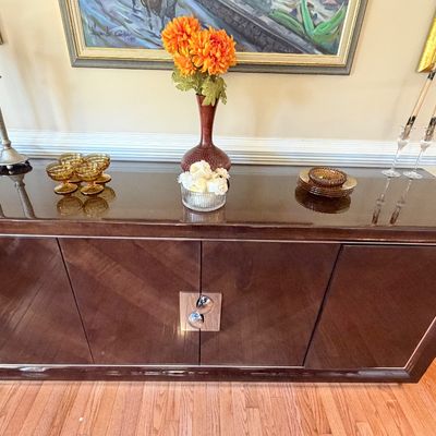 Sale Photo Thumbnail #108: High-gloss dark wood credenza featuring chevron patterned door fronts and central chrome hardware, displayed with amber glassware and decorative accents.