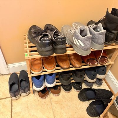 Sale Photo Thumbnail #160: A wooden shoe rack filled with various men's footwear, including Coach sneakers, Adidas athletic shoes, leather dress loafers, and work boots.