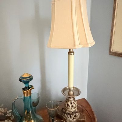 Sale Photo Thumbnail #276: Tall vintage table lamp with an ornate silver and gold base and beige fabric shade, sitting alongside a teal glass decanter with gold accents and matching glassware.