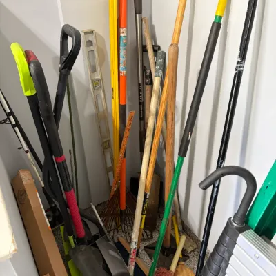 Sale Photo Thumbnail #24: Collection of assorted long-handled yard tools, levels, mops, brooms, and fishing rods stored in a corner.