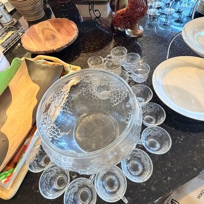 Sale Photo Thumbnail #100: Vintage pressed glass punch bowl set with grape pattern and matching cups arranged on a dark granite countertop.