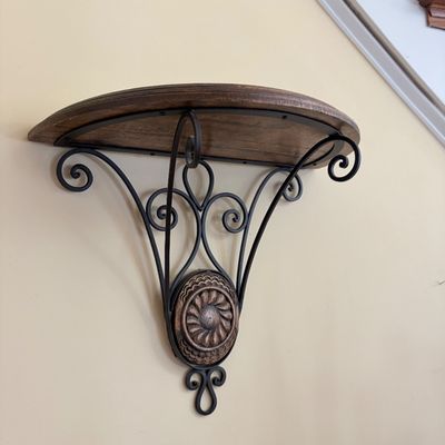 Sale Photo Thumbnail #142: Wall-mounted half-round shelf featuring a dark wood top supported by a wrought iron scrollwork base with a carved floral emblem accent.
