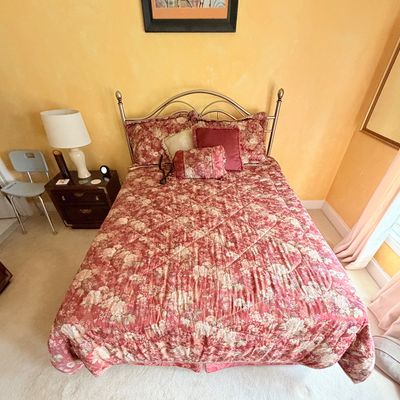 Sale Photo Thumbnail #279: Metal arch headboard bed dressed in a red and cream floral comforter, complete with matching shams and throw pillows.