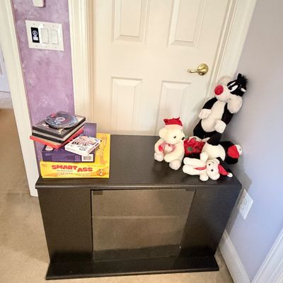 Sale Photo Thumbnail #297: Black wooden media cabinet holding a stack of board games and DVDs alongside plush toys, including Sylvester the Cat and holiday bears.